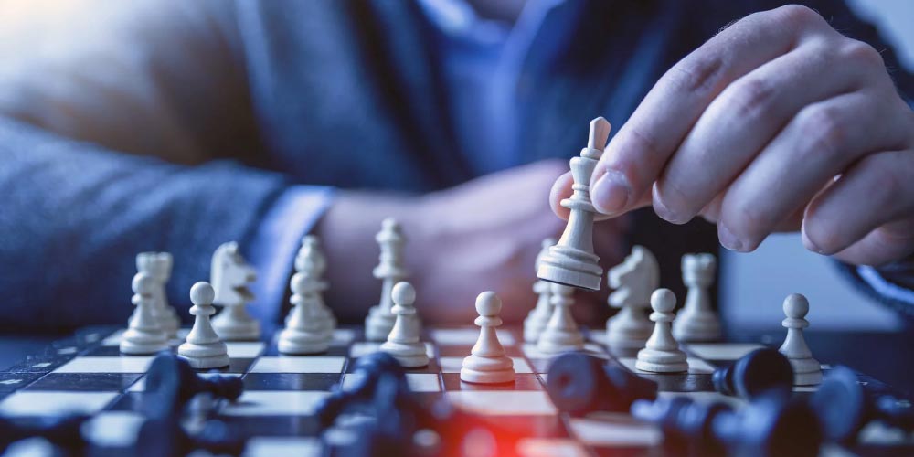 White man wearing sui playing chess, making a move with his Queen